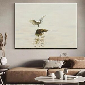 Puede incluir: Un p&aacute;jaro blanco con las alas extendidas se posa sobre una peque&ntilde;a roca en un cuerpo de agua. El agua est&aacute; tranquila y refleja el cielo y el p&aacute;jaro. El fondo es de color azul claro.