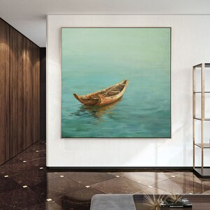 May include: A painting of a wooden boat floating on a calm, blue-green body of water. The boat is brown and has a light brown interior. The water is a light blue-green color and reflects the sky. The painting is framed in a simple, white frame.