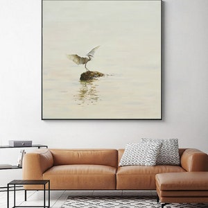 Puede incluir: Una pintura de acuarela de un p&aacute;jaro blanco con las alas extendidas de pie sobre una roca en un cuerpo de agua. El fondo es de color azul claro y el agua es de color azul claro con un toque de verde.