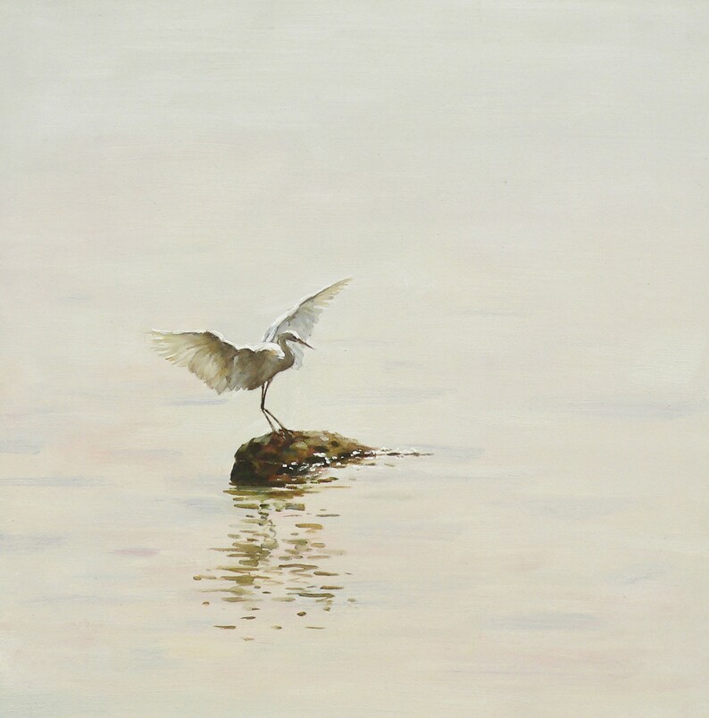 Puede incluir: Una garceta blanca con las alas extendidas se posa sobre una peque&ntilde;a roca en un cuerpo de agua. El agua est&aacute; tranquila y refleja la garceta y el cielo.