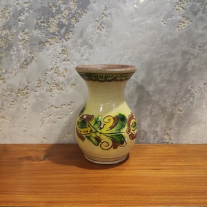 May include: A small, yellow ceramic vase with a brown rim and green and brown floral designs.