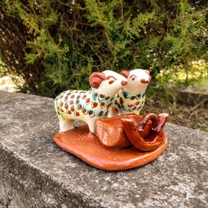 May include: Two ceramic sheep figurines with brown, white and green polka dots, standing on a brown ceramic cart with a handle.