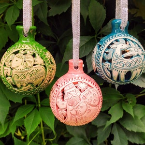 Op de afbeelding: Drie handgeschilderde keramische ornamenten met ingewikkelde ontwerpen. De ornamenten zijn groen, blauw en roze met witte details. Het groene ornament heeft een gestileerd dier, het blauwe ornament heeft een gestileerd dier en het roze ornament heeft een gestileerd persoon.
