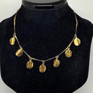 May include: A gold necklace featuring a fine chain and several circular pendants. The necklace is presented on a black mannequin, highlighting its design. The pendants are evenly spaced along the chain, creating a balanced look.