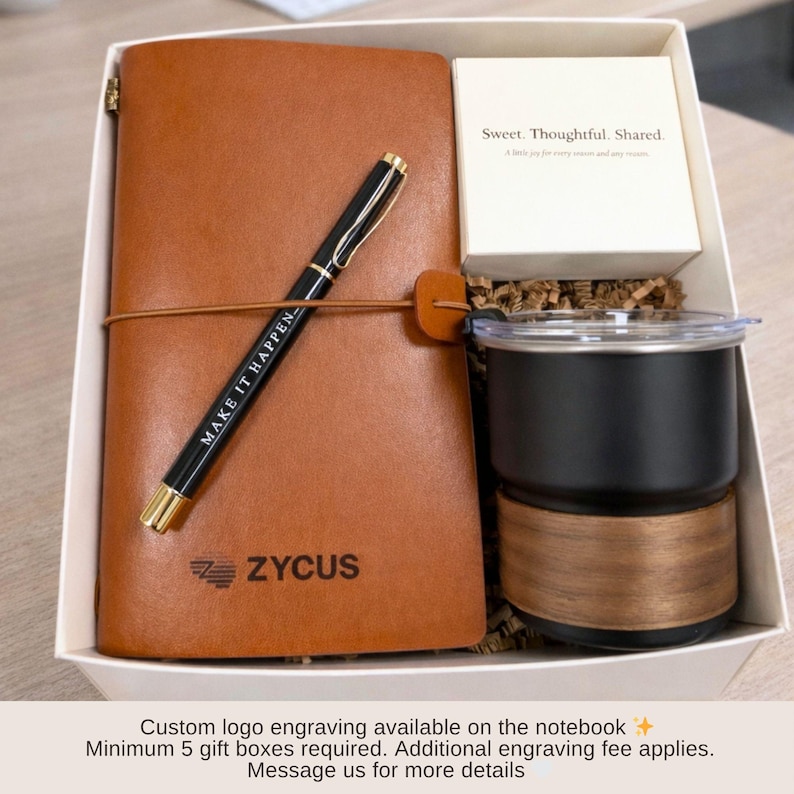 K&ouml;nnte beinhalten: Eine Geschenkbox mit einem braunen Lederjournal, einem schwarzen Stift mit der Aufschrift "MAKE IT HAPPEN", einem schwarzen Becher mit Holzsockel und einer kleinen wei&szlig;en Box. Das Journal hat das ZYCUS-Logo. Die wei&szlig;e Box hat den Text "Sweet. Thoughtful. Shared."