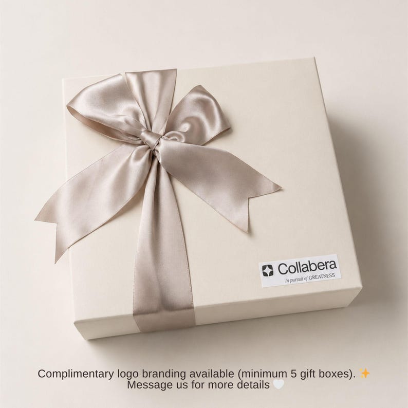 K&ouml;nnte beinhalten: Eine cremefarbene Geschenkbox, die mit einem Satinband und einer Schleife gebunden ist. Das Band hat eine hellbeige Farbe. Die Box hat einen kleinen wei&szlig;en Aufkleber mit dem Collabera-Logo und Text. Der Text unten lautet: Kostenloses Logo-Branding verf&uuml;gbar (mindestens 5 Geschenkboxen).