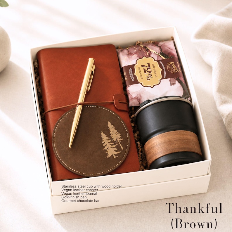 K&ouml;nnte beinhalten: Eine Geschenkbox mit der Aufschrift "Dankbar (Braun)" enth&auml;lt ein braunes veganes Lederjournal, einen goldenen Stift, einen Untersetzer mit Baumdesign, eine schwarze Edelstahl-Tasse mit Holzhalter und eine Gourmet-Schokoladen-Tafel.