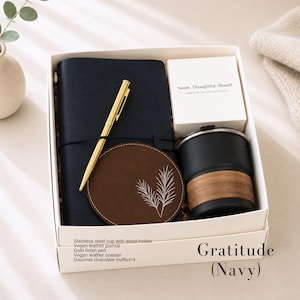 K&ouml;nnte beinhalten: Eine marineblaue Geschenkbox mit der Aufschrift "Gratitude (Navy)" enth&auml;lt ein marineblaues Notizbuch, einen goldenen Stift, einen braunen Untersetzer, eine schwarze Tasse mit Holzhalter und eine kleine wei&szlig;e Schachtel. Der Untersetzer hat ein wei&szlig;es Blattdesign.