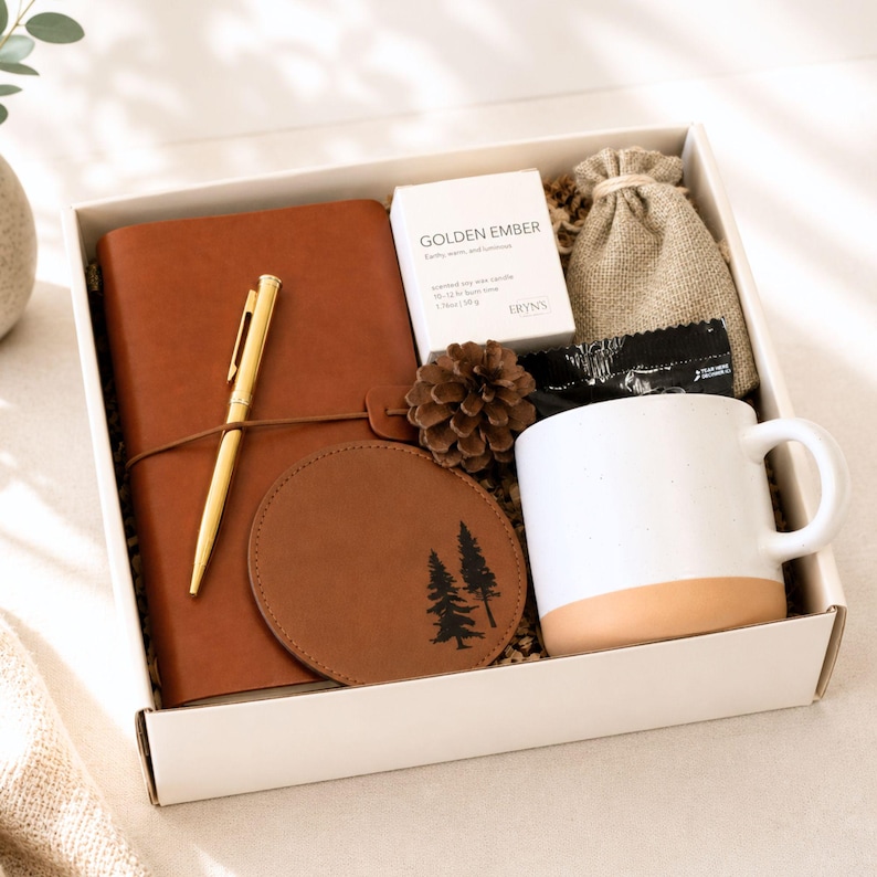 Puede incluir: Una caja de regalo que contiene un diario de cuero marr&oacute;n con un bol&iacute;grafo dorado, un posavasos redondo marr&oacute;n con estampado de pino, una taza de cer&aacute;mica blanca y beige, una pi&ntilde;a, una peque&ntilde;a bolsa de arpillera y una vela Golden Ember.