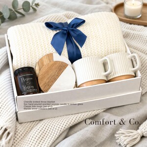 Puede incluir: Una caja de regalo que contiene una manta de punto de chenilla color crema atada con una cinta azul marino, dos tazas de cer&aacute;mica blanca acanalada, dos posavasos redondos de m&aacute;rmol y madera, y una vela de 5oz en vidrio &aacute;mbar.