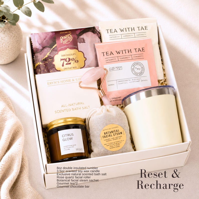 May include: A gift box containing an 8oz double insulated tumbler, a 3.5oz scented soy wax candle labeled Citrus Glow, a rose quartz facial roller, a botanical facial steam sachet, two Tea With Tae tea packets, and a Rogers 72% dark chocolate bar.
