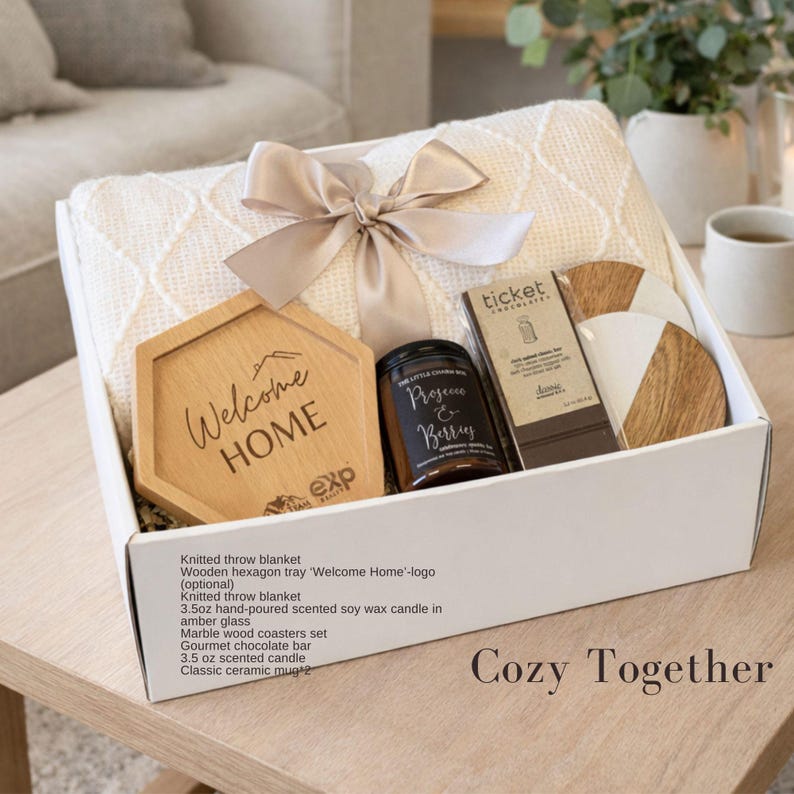 Puede incluir: Una caja de regalo que contiene una manta de punto color crema atada con una cinta beige, una bandeja de madera hexagonal con el texto Welcome HOME, una vela de vidrio &aacute;mbar de 3.5 oz etiquetada Prosecco & Berries, chocolate Ticket y posavasos.