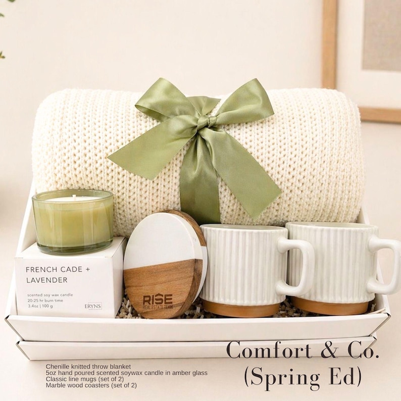 Puede incluir: Un set de regalo que incluye una manta de chenilla color crema atada con una cinta verde salvia, una vela de cera de soja de 100g, dos tazas de cer&aacute;mica blanca acanalada y un posavasos redondo de m&aacute;rmol y madera.