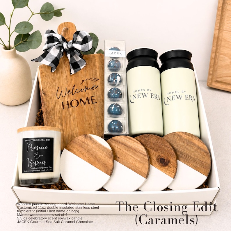 Puede incluir: Una caja de regalo con una tabla de madera con el texto 'Welcome HOME' y un lazo a cuadros blanco y negro, chocolates JACEK, dos vasos aislados color crema de 11 oz con 'HOMES BY NEW ERA', cuatro posavasos de m&aacute;rmol y madera, y una vela de 5,5 oz.