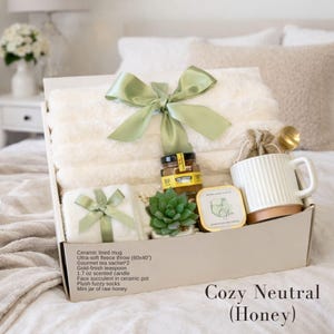 Puede incluir: Una caja de regalo que contiene una manta de forro polar blanca con una cinta verde salvia, una taza de cer&aacute;mica blanca, un tarro de miel, una vela arom&aacute;tica, una suculenta artificial en maceta de cer&aacute;mica y una cucharilla dorada.