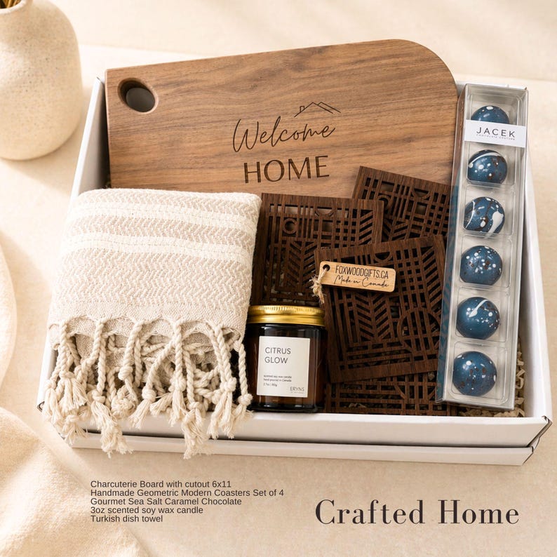 Puede incluir: Una caja de regalo que contiene una tabla de madera con un recorte y el texto Welcome HOME, un pa&ntilde;o de cocina beige con flecos, cuatro posavasos geom&eacute;tricos de madera oscura, una vela de soja Citrus Glow y seis bombones de caramelo salado.