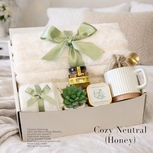 May include: A gift box containing a 60x40 inch ultra-soft fleece throw with a green ribbon, a ceramic lined mug, a gold-finish teaspoon, a 1.7 oz scented candle, a faux succulent in a ceramic pot, plush fuzzy socks, and a mini jar of raw honey.