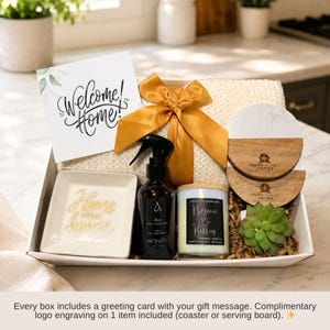 Puede incluir: Una caja de regalo que contiene una tarjeta blanca con el texto Welcome Home, una manta de punto color crema con un lazo dorado, un plato cuadrado blanco con texto dorado Home sweet home, un pulverizador negro, una vela, dos posavasos y una suculenta.