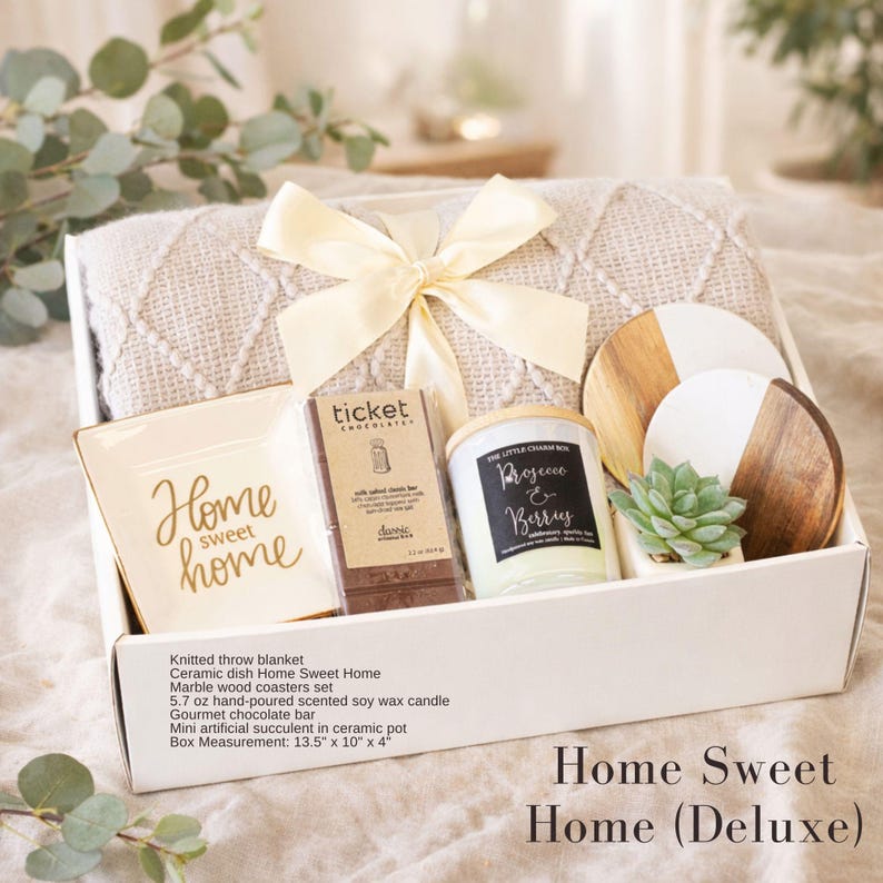 Puede incluir: Una caja de regalo que contiene una manta de punto beige con un lazo color crema, un plato de cer&aacute;mica cuadrado con el texto Home sweet home, una barra de chocolate Ticket, una vela Prosecco & Berries, dos posavasos de m&aacute;rmol y madera y una suculenta.