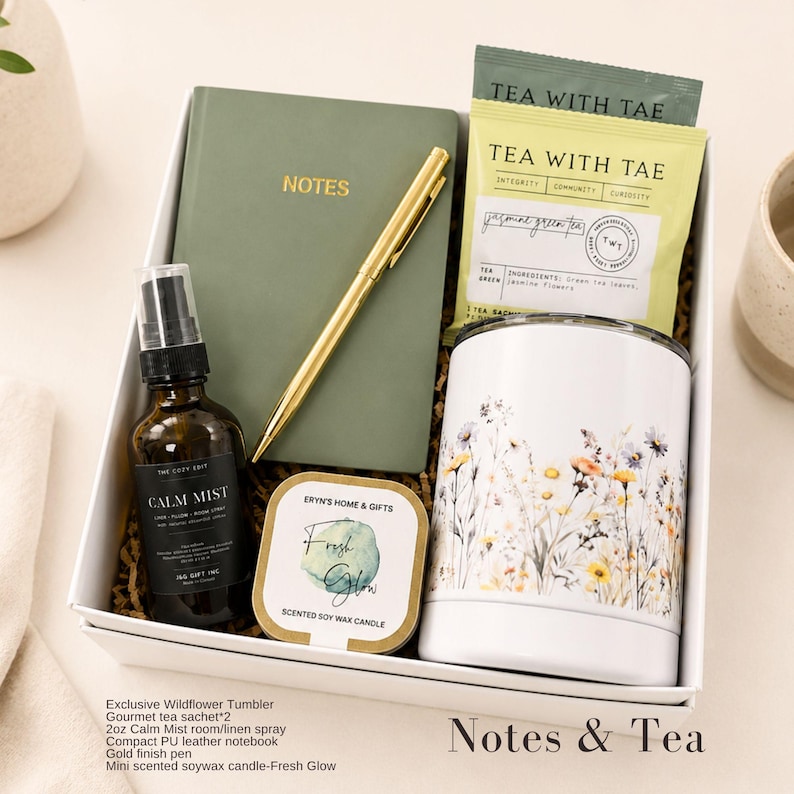 May include: A gift box containing a sage green notebook with the word NOTES, a gold pen, two Tea With Tae jasmine green tea sachets, a 2oz amber glass bottle of Calm Mist spray, a Fresh Glow soy candle, and a white tumbler with wildflower print.