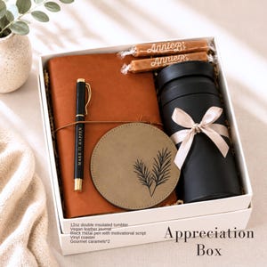 Puede incluir: Una caja de regalo que contiene un diario de cuero vegano color canela, un bol&iacute;grafo de metal negro con el texto MAKE IT HAPPEN, un posavasos redondo de vinilo verde oliva con estampado de hojas, un vaso t&eacute;rmico negro de 355ml con lazo beige.