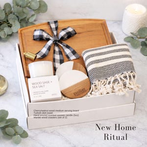 Puede incluir: Un set de regalo que incluye una tabla de servir de madera de cerezo y nogal con un lazo de cuadros blanco y negro, un pa&ntilde;o de cocina turco a rayas, una vela de cera de soja de 150g Wood Sage and Sea Salt y dos posavasos de m&aacute;rmol y madera.