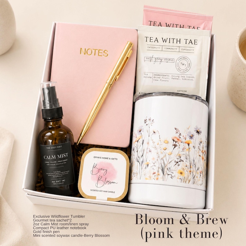 May include: A gift box containing a pink notebook with the word NOTES in gold, a gold pen, two Tea With Tae tea sachets, a white tumbler with a wildflower print, a brown glass bottle of Calm Mist spray, and a Berry Blossom scented soy wax candle.