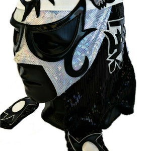 May include: A black and white wrestling mask with a silver sequined design. The mask has a black and white star on the forehead and a black and white design on the side. The mask has a black and white design on the back.