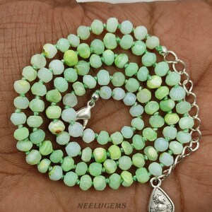 May include: A green opal gemstone necklace with faceted beads and a silver clasp. The necklace is strung on a green cord and has a silver pendant with a design.