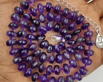 May include: A purple amethyst gemstone necklace with a silver clasp and a silver chain. The necklace is made of small, round beads that are strung together on a purple cord.