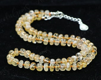 May include: A long necklace made of light yellow and clear beads with a silver clasp. The beads are strung on a thin brown cord.