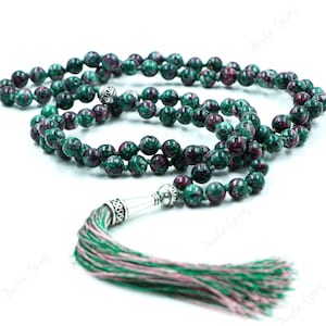 以下が含まれることがあります： 緑とピンクの祈りのビーズマラ、シルバーのタッセル付き。ビーズはピンクの斑点のある緑の石で作られています。