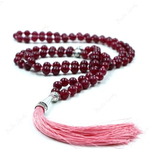 以下が含まれることがあります： ピンクのタッセルが付いた、マルーン色の数珠。ビーズは丸くて滑らかです。