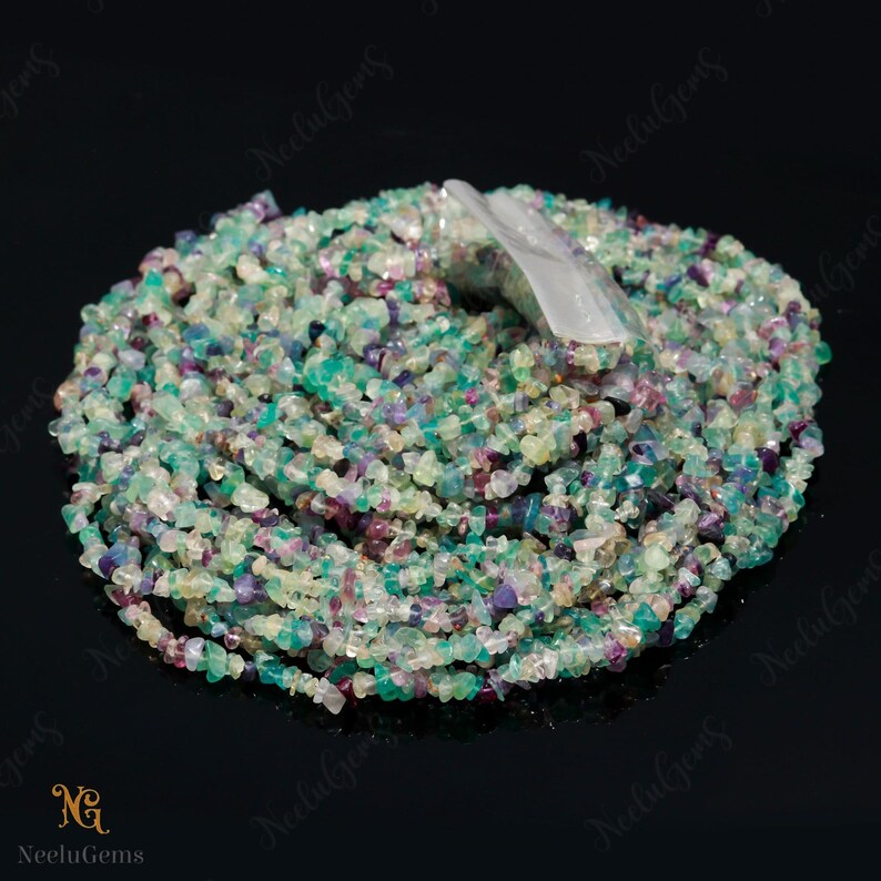 May include: A strand of multi-colored chip gemstone beads. The beads are a mix of green, blue, purple, and white. The beads are small and irregular in shape.