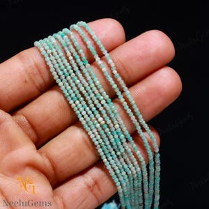 May include: A strand of light blue and green gemstone beads. The beads are small and round, and they are strung on a thin wire. The beads are arranged in a straight line, and they are all the same size.