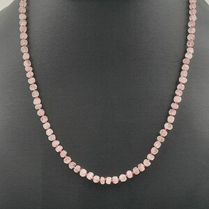 May include: A pink rose quartz beaded necklace with a pink thread. The necklace is displayed on a black mannequin bust. The text "NEELUGEMS" is visible on the bust.