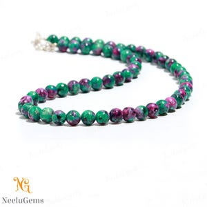 May include: A green and pink gemstone bead necklace. The beads are round and have a marbled pattern.