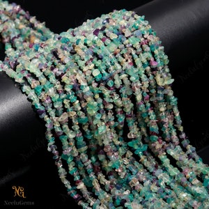 May include: A strand of multi-colored chip beads. The beads are a mix of green, blue, purple, and white. The beads are small and irregular in shape. The beads are strung on a clear thread.