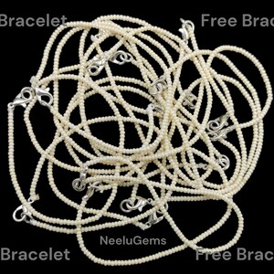May include: A pile of white beaded bracelets with silver clasps. The bracelets are all the same length and are arranged in a random pattern. The text "Free Bracelet" appears four times around the edge of the image. The text "NeeluGems" appears in the center of the image.