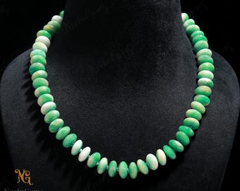 May include: A beaded necklace featuring a strand of oval-shaped beads in shades of green and white. The necklace is displayed on a black mannequin, showcasing the jewelry's design and color variations. The beads are strung together with a light green cord.