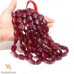 Può includere: Una collana di perle ovali di pietra preziosa di colore rosso scuro. Le perle sono lisce e lucidate e sono infilate su un cordoncino rosso.
