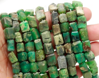 Könnte beinhalten: Eine Strähne aus grünen, braunen und grauen Edelsteinperlen. Die Perlen sind facettiert und haben eine raue, natürliche Textur. Die Perlen sind etwa 10 mm groß.