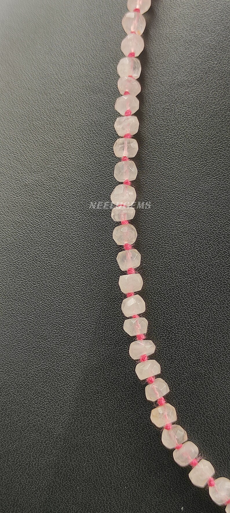 May include: A strand of faceted, clear pink quartz beads strung on pink thread. The beads are approximately 6mm in diameter.