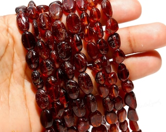 May include: A strand of dark red gemstone beads, each bead is oval shaped and has a smooth, polished finish. The beads are strung together on a clear thread.