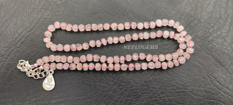May include: A pink rose quartz gemstone necklace with a silver pendant. The necklace is made of small, faceted beads and is strung on a pink thread.