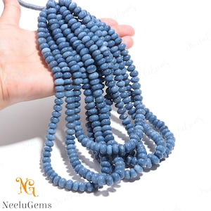May include: A strand of blue gemstone beads, approximately 6mm in diameter, with a slightly irregular shape. The beads are strung on a clear thread and are arranged in a loose pile.