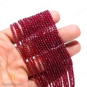 May include: A strand of red gemstone beads. The beads are faceted and have a shiny finish. The beads are strung on a clear thread.