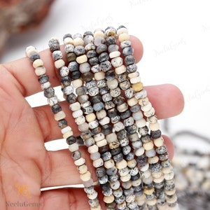 May include: A strand of white, gray, and black gemstone beads. The beads are round and have a speckled pattern. The beads are strung on a clear thread.