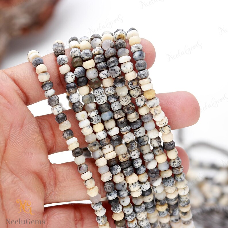 May include: A strand of white, gray, and black gemstone beads. The beads are round and have a speckled pattern. The beads are strung on a clear thread.