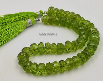 May include: A strand of faceted, olive-green peridot beads with a bright green tassel on each end. The tassels are made of fine threads and have silver-colored caps. The beads are arranged in a necklace or bracelet style.